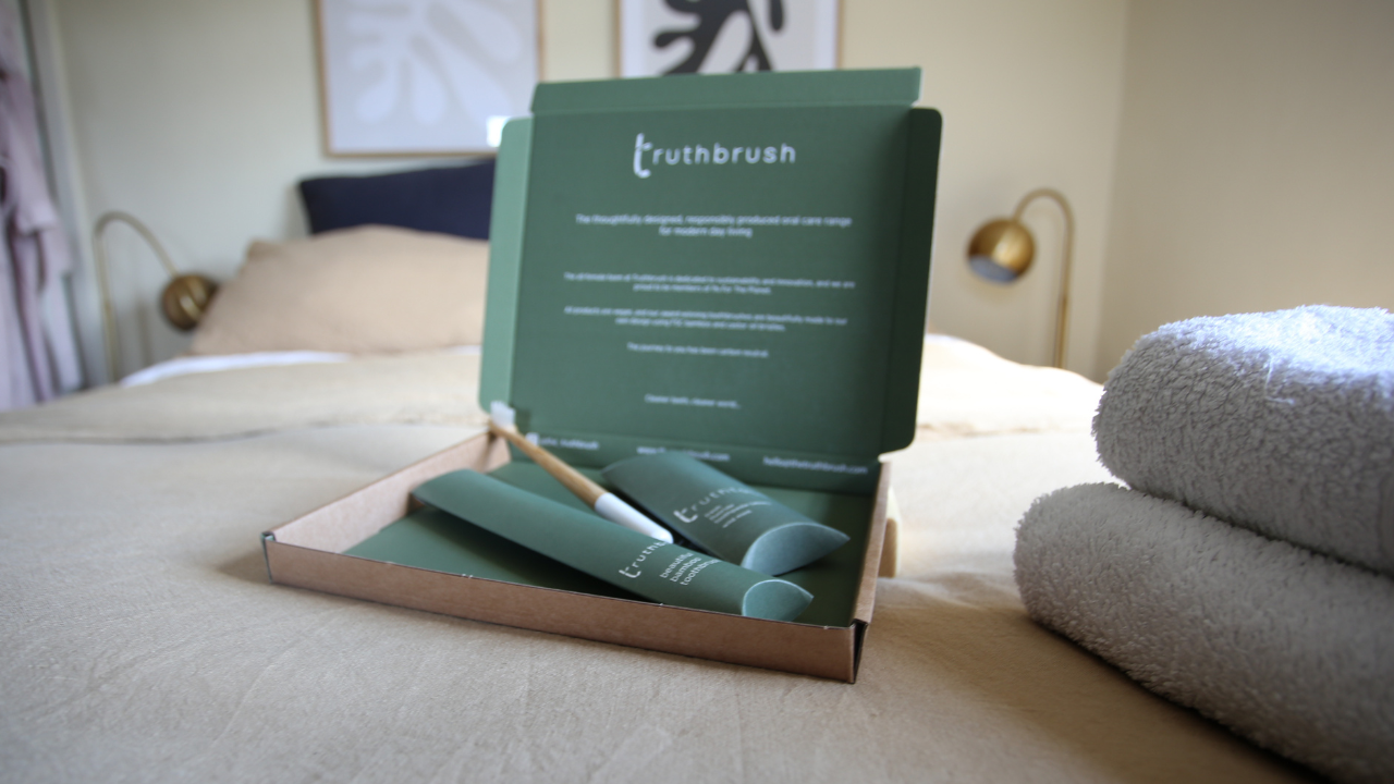 Open branded box of Truthbrush products, on a natural linen dressed bed in a bohemian bedroom